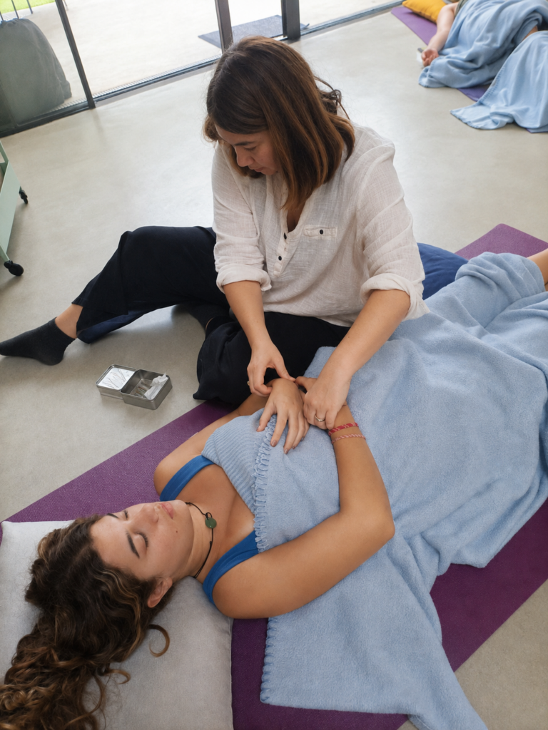 Dona estirada sobre una estoreta durant una sessió d'acupuntura comunitària mentre la terapeuta pren el pols