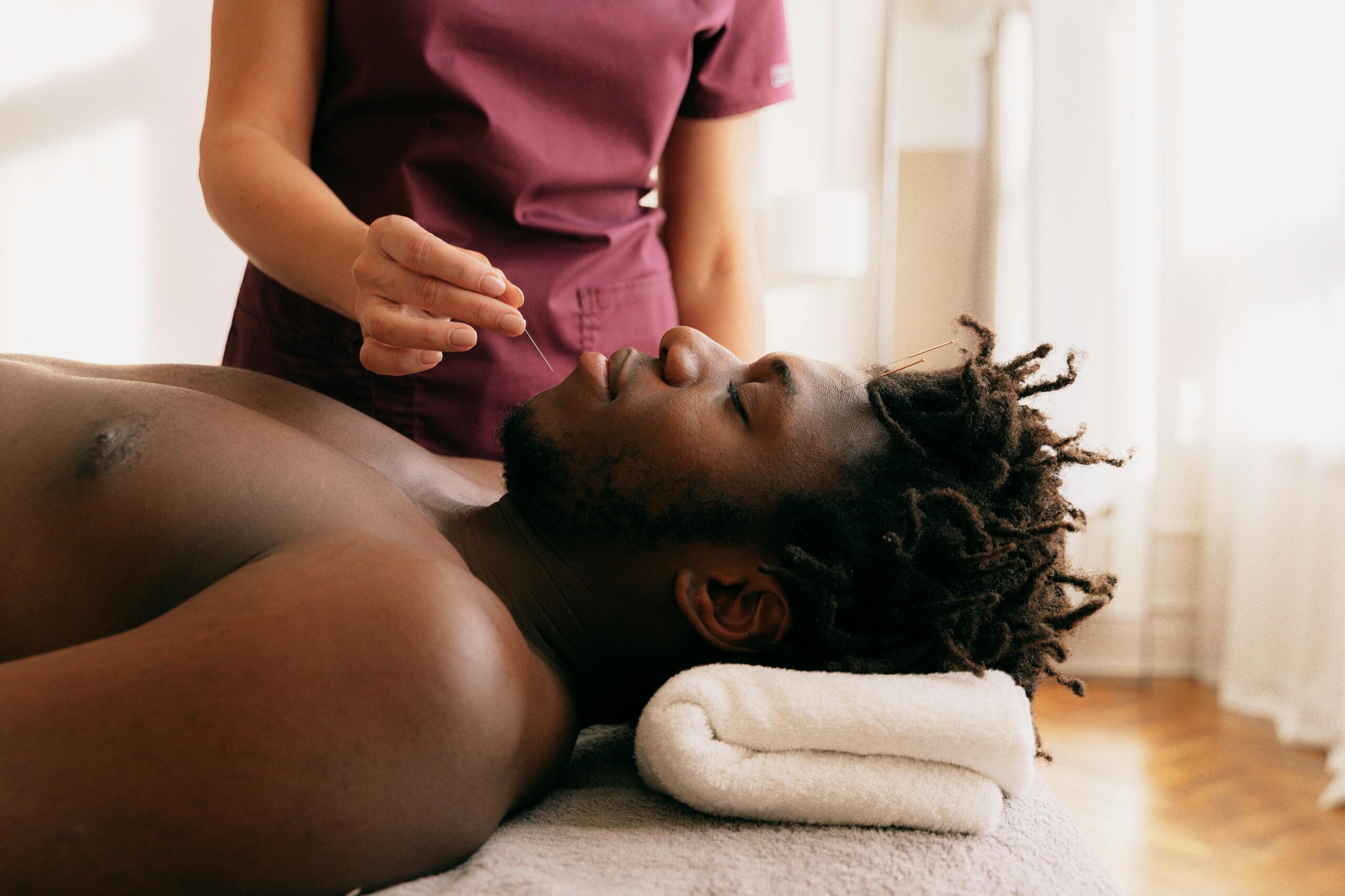 Terapeuta aplicando acupuntura facial a un paciente durante una sesión.