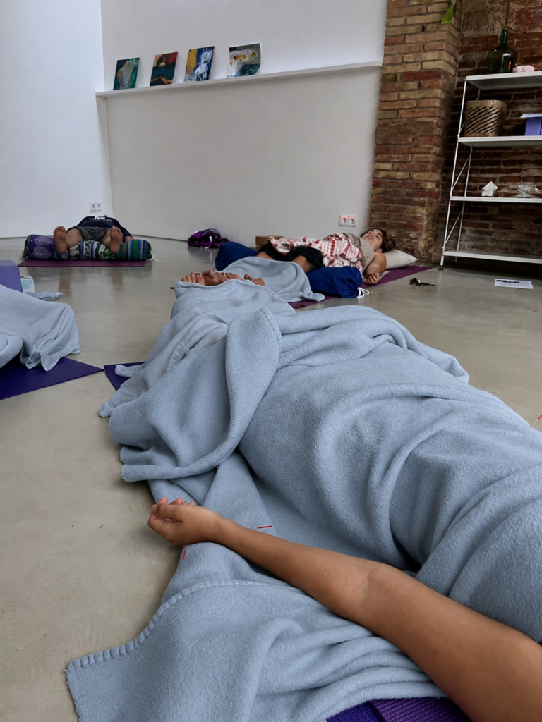 Persones rebent acupuntura comunitària en estoretes de ioga, cobertes amb mantes.